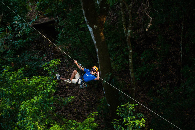 Guest in a helmet riding a zipline through the forest at Canopy Mal País
