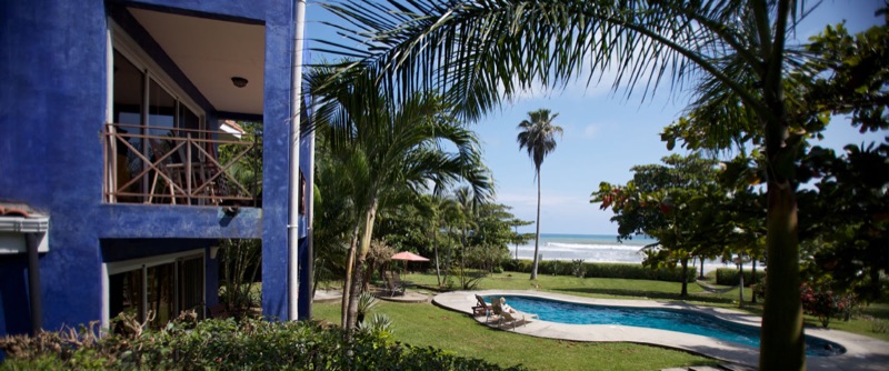 Blue hotel building beside a pool and lawn with the beach beyond at Hotel Casa Azul