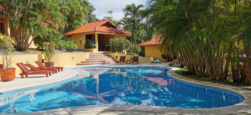 Pool with loungers in front of orange-roofed bungalows at Hotel Ritmo Tropical